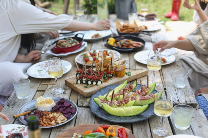 "Sommerliche Picknickszene mit Personen am Tisch und vielfältigen Speisen"