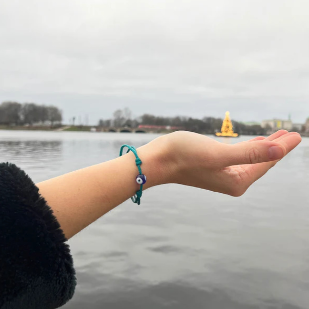 Junge Frau mit türkisfarbenem Upcycling-Armband am Handgelenk, See im Hintergrund